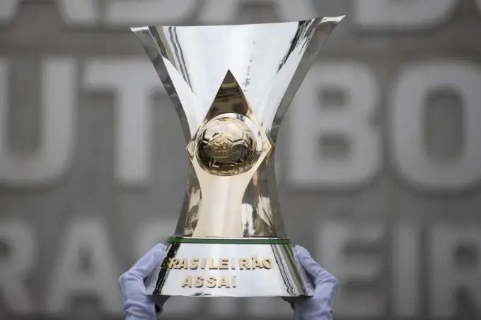 Tabela do Brasileirão 2023 é divulgada pela CBF; Confira - Taça do Campeonato Brasileiro, erguida por mãos usando luvas