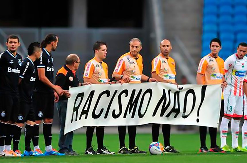 Jogadores e trio de arbitragem seguram faixa que exibe frase "racismo não"