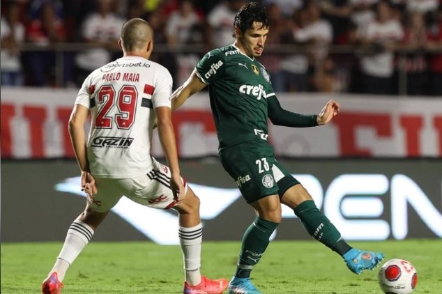 Jogador do São Paulo, de costas, e jogador do Palmeiras, de frente, tocando a bola com a ponta do pé esquerdo, durante clássico Choque-Rei