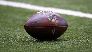 Bola de futebol americano, com logo da NFL, posicionada em gramado verde