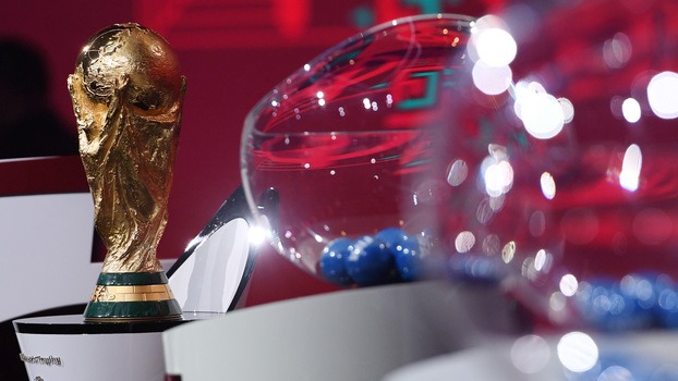 Taça da Copa do Mundo ao lado de pote para sorteio dos grupos da primeira fase do mundial