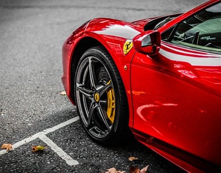 Parte lateral frontal de Ferrari vermelha, com pneu preto e detalhe da marca em amarelo