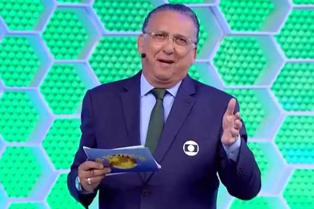 Narrador Galvão Bueno, de terno e gravata, diante de fundo verde de transmissão da Glob
