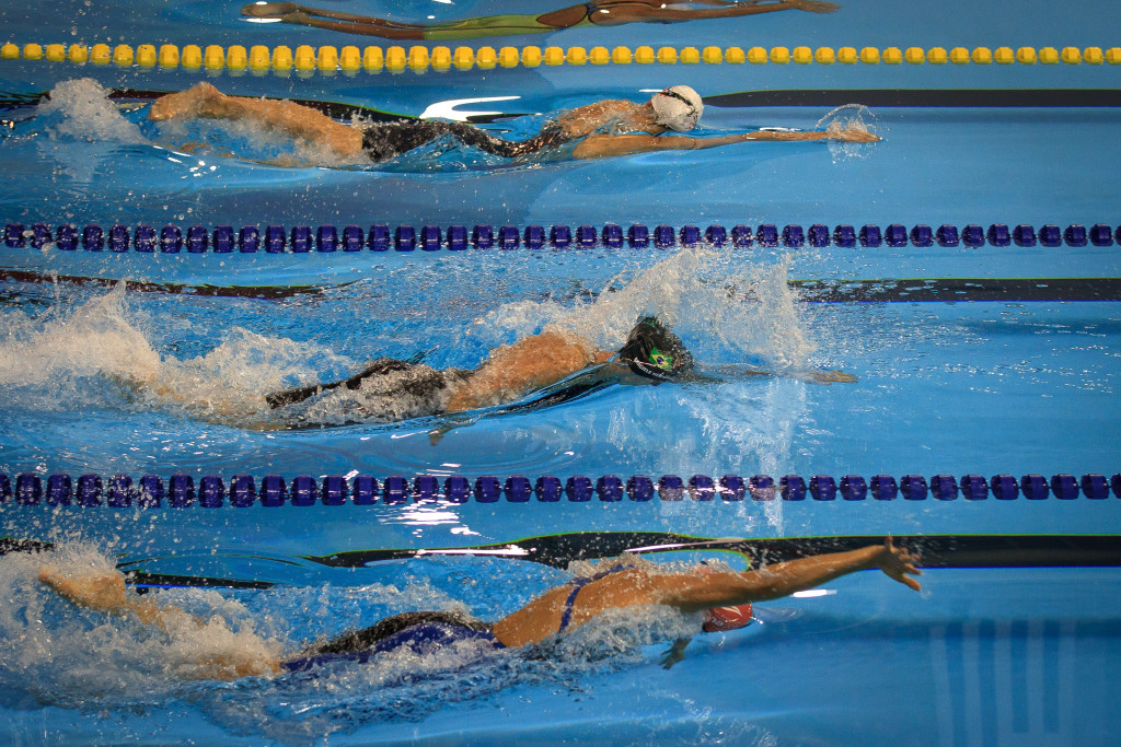 Três nadadoras durante prova em piscina, cada uma em uma raia
