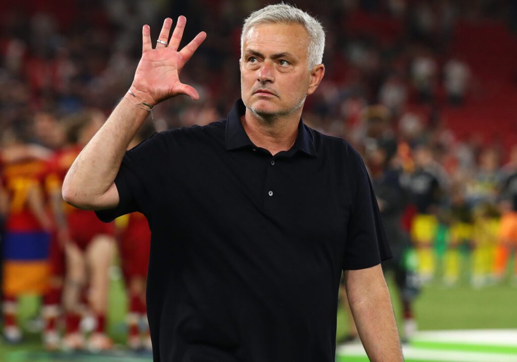 José Mourinho fazendo o sinal de número 5 com a mão direita e vestindo camisa preta.