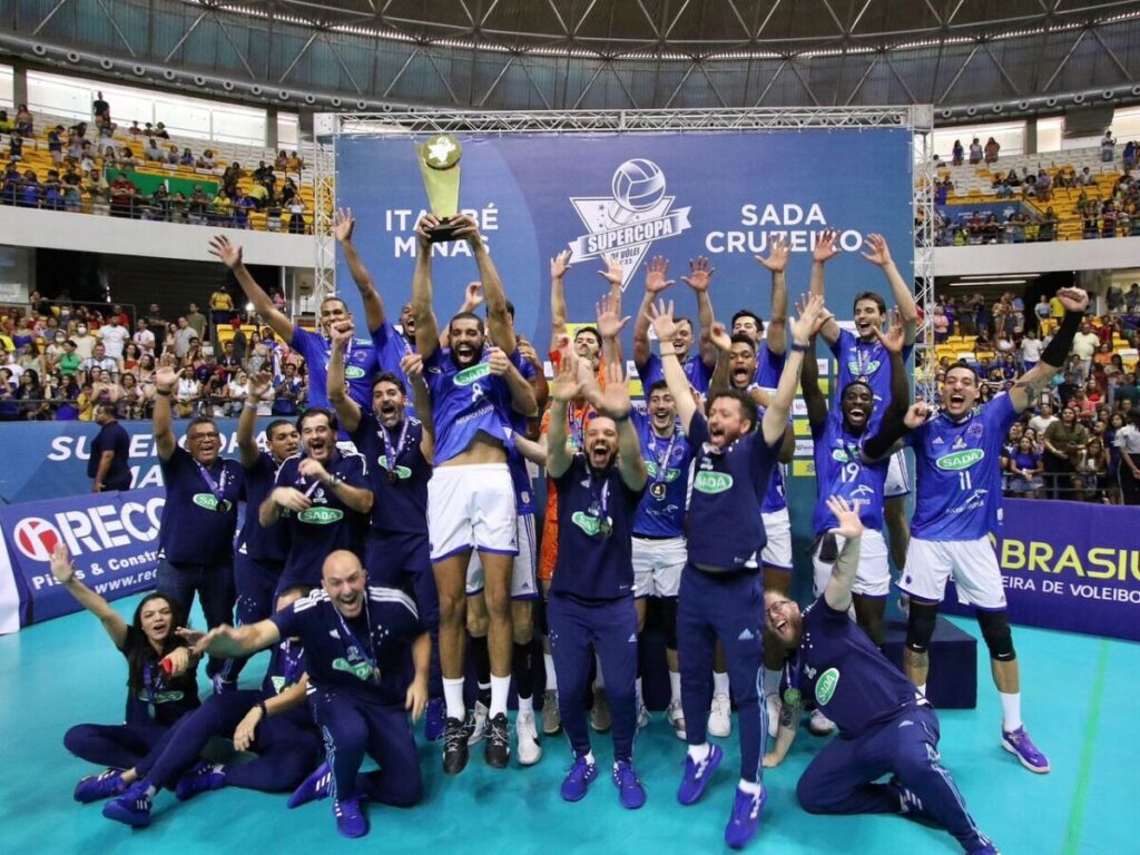 Equipe do Sada Cruzeiro comemorando conquista de campeonato. Atletas em festa e capitão do time erguendo a taça.