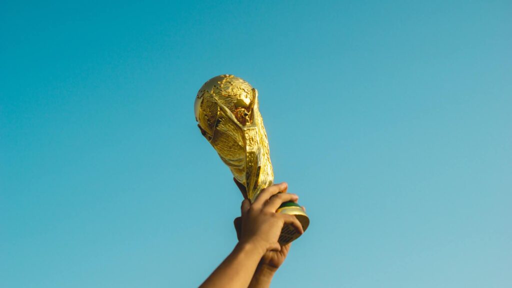 Novo formato da Copa do Mundo: Em contra-plongeé, taça da Copa do Mundo sendo erguida por mãos