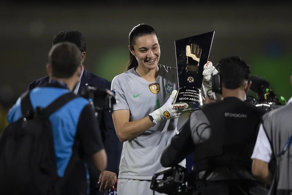 A goleira da Seleção Brasileira, Lorena, está sorrindo e segurando a taça de melhor goleira da Copa América.