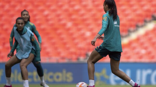 Seleção Brasileira faz último treino. Duas jogadoras aparecem em campo com a bola nos pés. Elas estão de costas e vestem uniformes azuis.