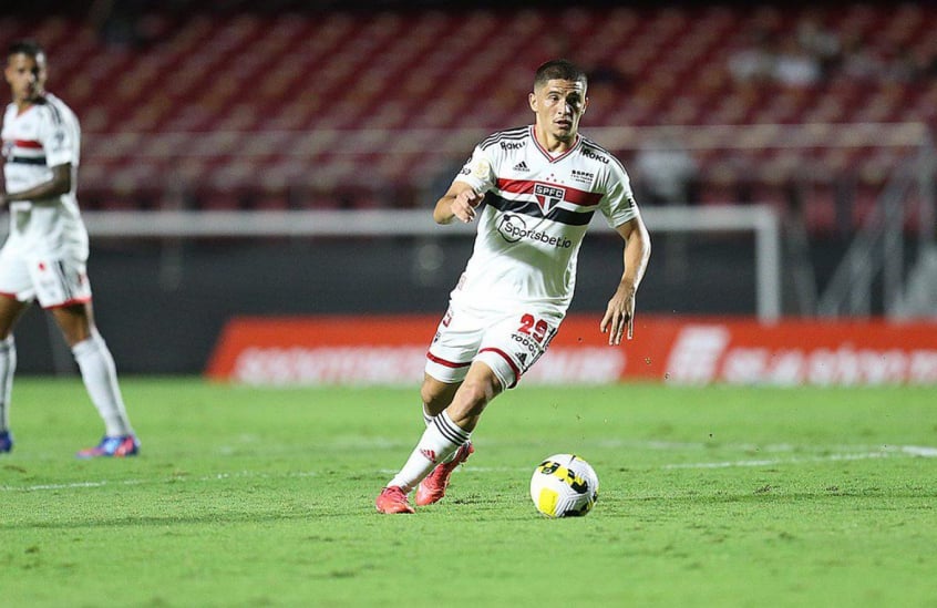 São Paulo renova com Pablo Maia. Jogador aparece em campo correndo atrás da bola. Ele veste uniforme branco com listras horizontais em vermelho e preto.