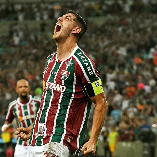 Fluminense vence The Strongest. Jogador aparece em primeiro plano com a cabeça levantada gritando ao comemorar o gol. Ele veste uniforme em três cores: verde, vermelho escuro e com detalhes em branco.