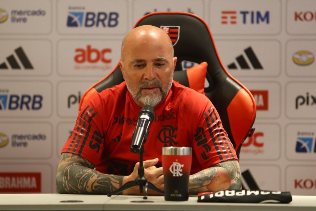 "Decidi ficar aqui", diz Sampaoli no Flamengo em apresentação - Sampaoli está sentado na mesa, de frente pra uma bancada na sala de entrevistas do Flamengo
