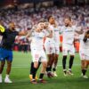 Sevilla vence Manchester United. Jogadores aparecem abraçados comemorando a classificação. Eles aparecem com uniforme branco com detalhes em vermelho.