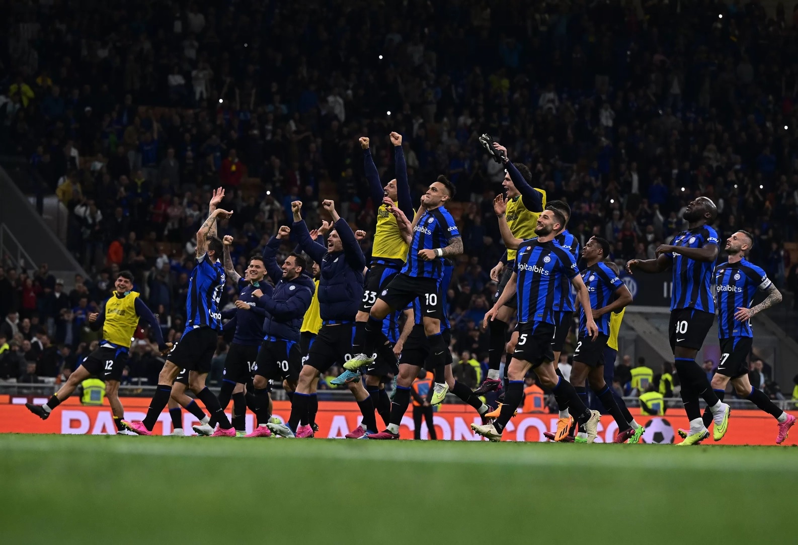 Inter de Milão vai à final da Copa Itália. Jogadores estão no centro de campo. Todos pulam e gritam comemorando a classificação da equipe. Eles vestem uniforme azul com listras verticais pretas e calção preto.