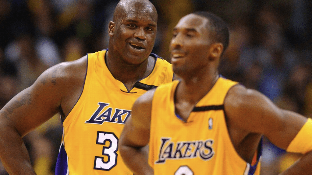 Shaquille O'Neal em quadra defendendo a camisa dos Lakers. O Jogador está sorrindo e bastante suado pelo jogo
