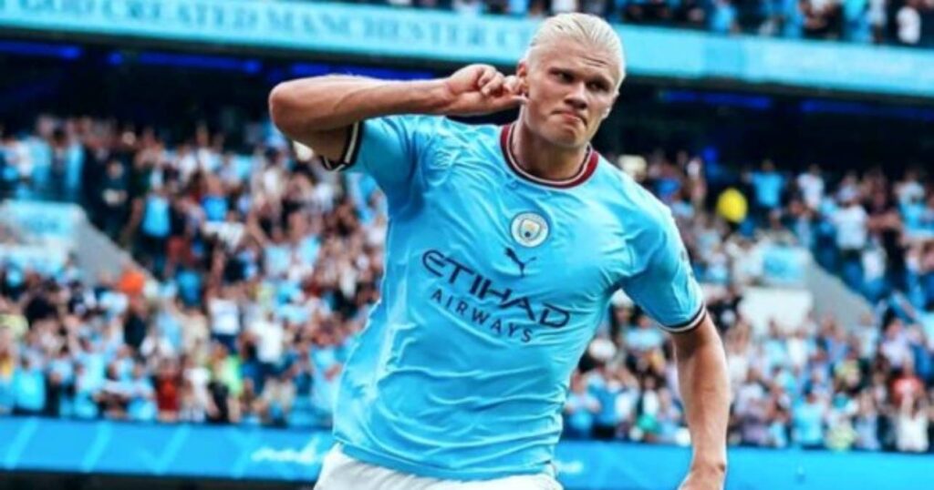 Haaland se torna o maior artilheiro da Premier League em uma edição - Haaland corre com a mão direita na orelha direita, comemorando gol marcado pelo Manchester City