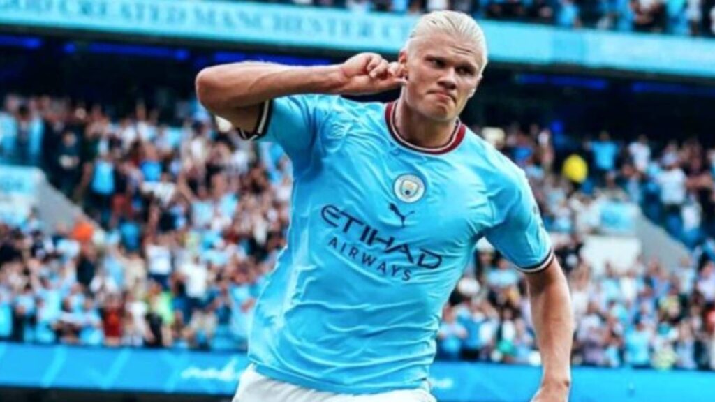 Haaland se torna o maior artilheiro da Premier League em uma edição - Haaland corre com a mão direita na orelha direita, comemorando gol marcado pelo Manchester City