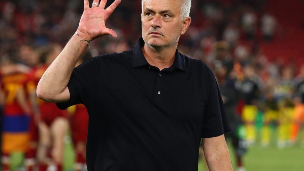 José Mourinho fazendo o sinal de número 5 com a mão direita e vestindo camisa preta.