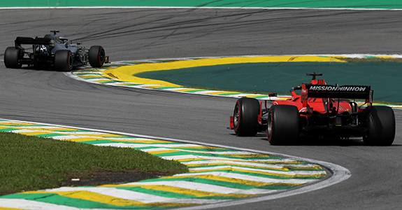 Carros de fórmula 1 fazendo curva em pista de corrida.