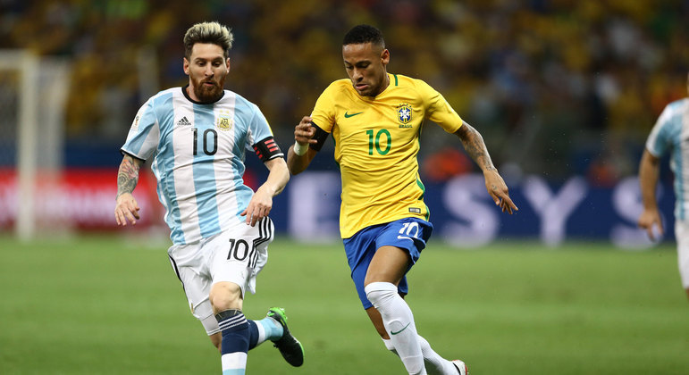 Eliminatórias da Copa do Mundo: Messi, vestindo camisa listrada azul e branca e short branco do uniforme da Seleção Argentina, disputando bola com Neymar, que veste short azul e blusa amarela da Seleção Brasileira.