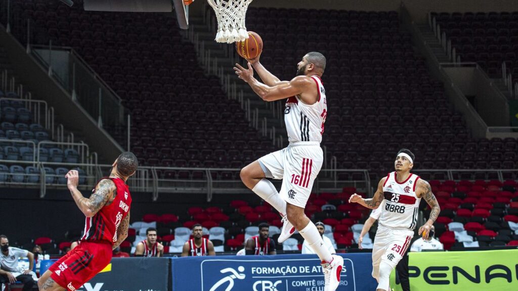Jogador do Flamengo, registrado ainda no ar, com bola de basquete na mão, para marcar cesta para o seu time. Termos mais comuns do basquete.