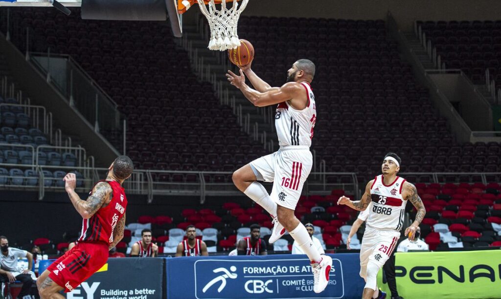 Jogador do Flamengo, registrado ainda no ar, com bola de basquete na mão, para marcar cesta para o seu time. Termos mais comuns do basquete.