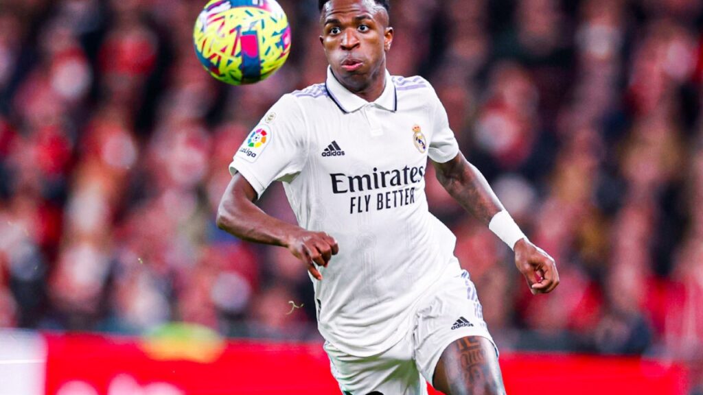 Vinícius Júnior em partida pelo Real Madrid, acompanhando a bola que quica na sua frente