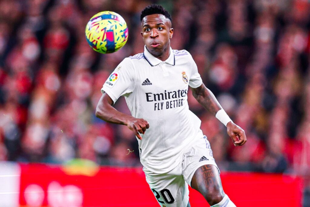 Vinícius Júnior em partida pelo Real Madrid, acompanhando a bola que quica na sua frente