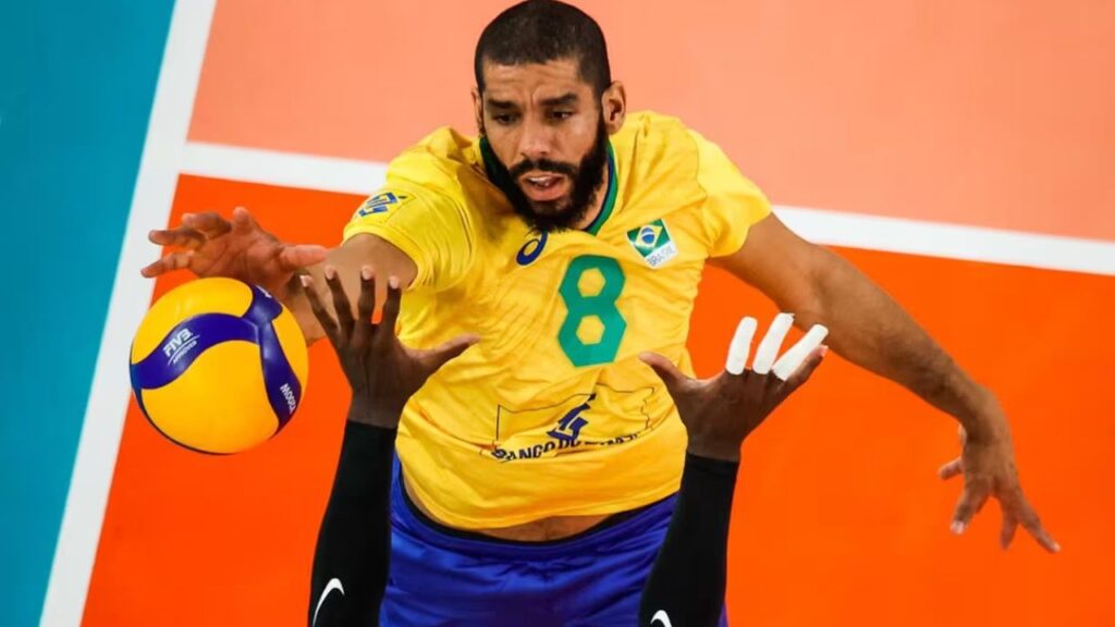 Conselho de Ética Anuncia Suspensão De Wallace. Jogador aparece em primeiro plano com a camisa amarela em detalhes verde. Ele joga vôlei e tenta passar a bola com as mãos enquanto salta.