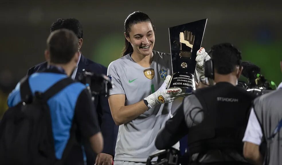 A goleira da Seleção Brasileira, Lorena, está sorrindo e segurando a taça de melhor goleira da Copa América.
