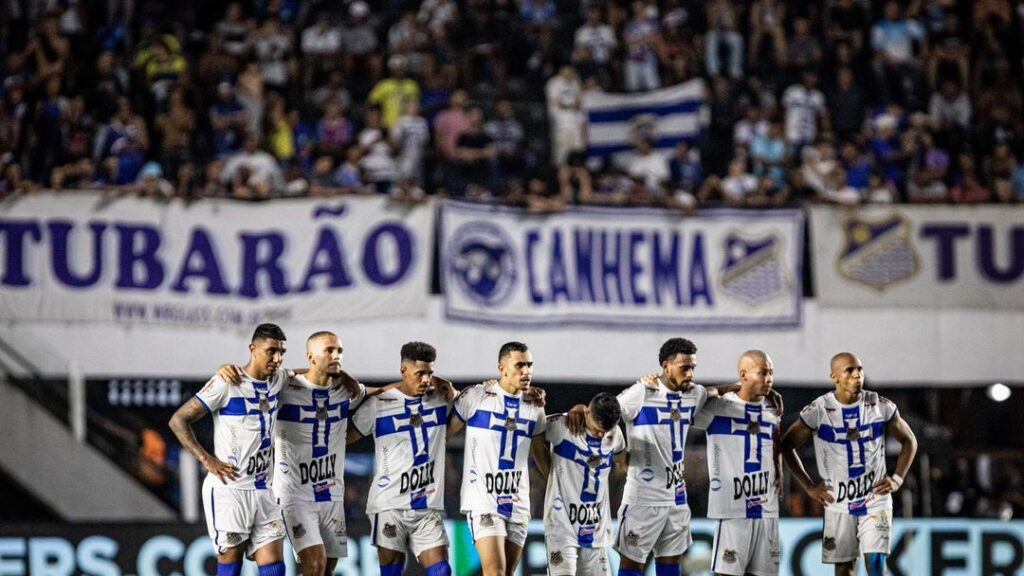 Os jogadores do Água Santa aparecem um ao lado do outro e olham para a meta do gol aguardando a cobrança de pênaltis.