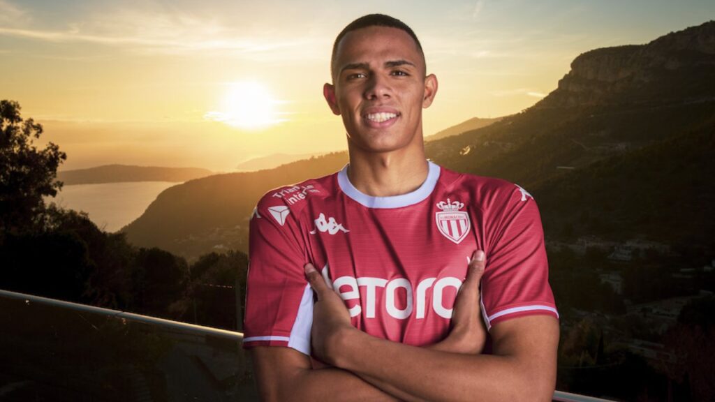 Lateral direito Monaco posa com camisa do Monaco em frente a paisagem montanhosa