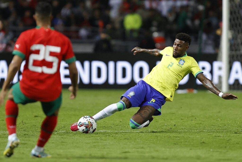 Em jogo do Brasil, Emerson Royal tem lesão no joelho e passará por cirurgia - Lateral do Brasil, Emerson Royal dá carrinho na bola enquanto jogador do Marrocos o observa