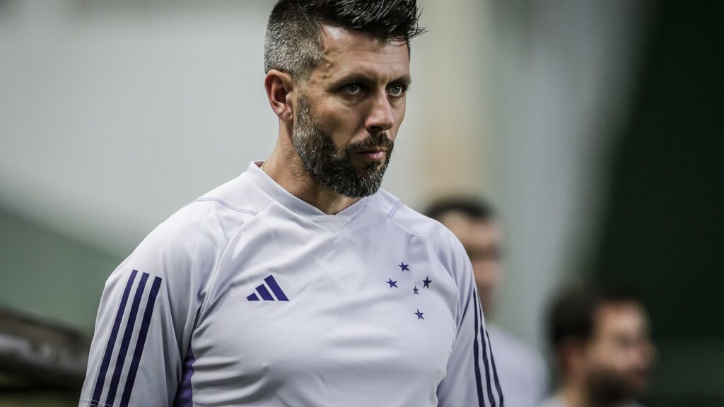 Homem aparece concentrado olhando para algo. Ele veste camiseta branca, com detalhes em azul.