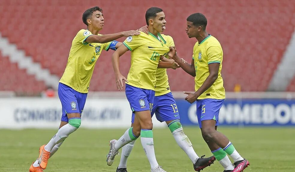 Seleção Brasileira vence Paraguai. Três garotos aparecem na imagem. Eles estão comemorando gols e vestem uniforme com camiseta amarela em detalhes em verde, e shorts azul com detalhes em branco.