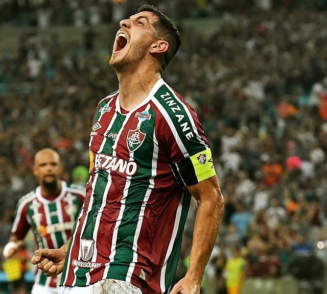 Fluminense vence The Strongest. Jogador aparece em primeiro plano com a cabeça levantada gritando ao comemorar o gol. Ele veste uniforme em três cores: verde, vermelho escuro e com detalhes em branco.