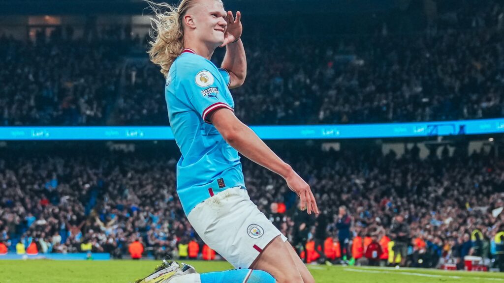 Haaland se torna o maior artilheiro da Premier League em uma edição - Jogador aparece ajoelhado no gramado. Ele veste uniforme azul com calção branco e está com cabelos loiros e soltos.