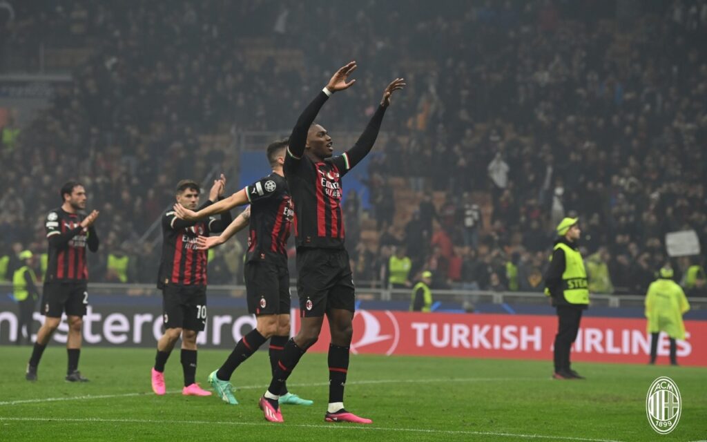 Milan vence Napoli. No primeiro plano da imagem, o jogador aparece comemorando o gol com os braços levantados. Ele veste uniforme preto com detalhes em vermelho e branco.