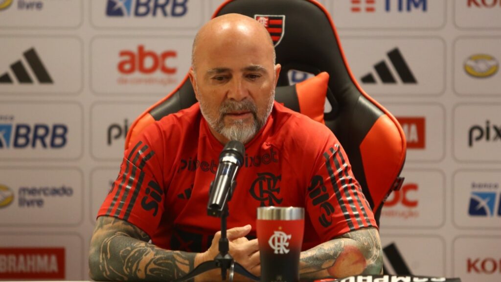 "Decidi ficar aqui", diz Sampaoli no Flamengo em apresentação - Sampaoli está sentado na mesa, de frente pra uma bancada na sala de entrevistas do Flamengo