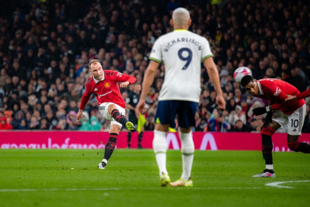 Tottenham e Manchester United empatam em jogão pela Premier League - Eriksen, do Manchester United, finaliza para o gol. A bola bate em Rashford, seu companheiro de equipe. Enquanto que Richarlison, do Tottenham, está de costas para a câmera e observa o lance.