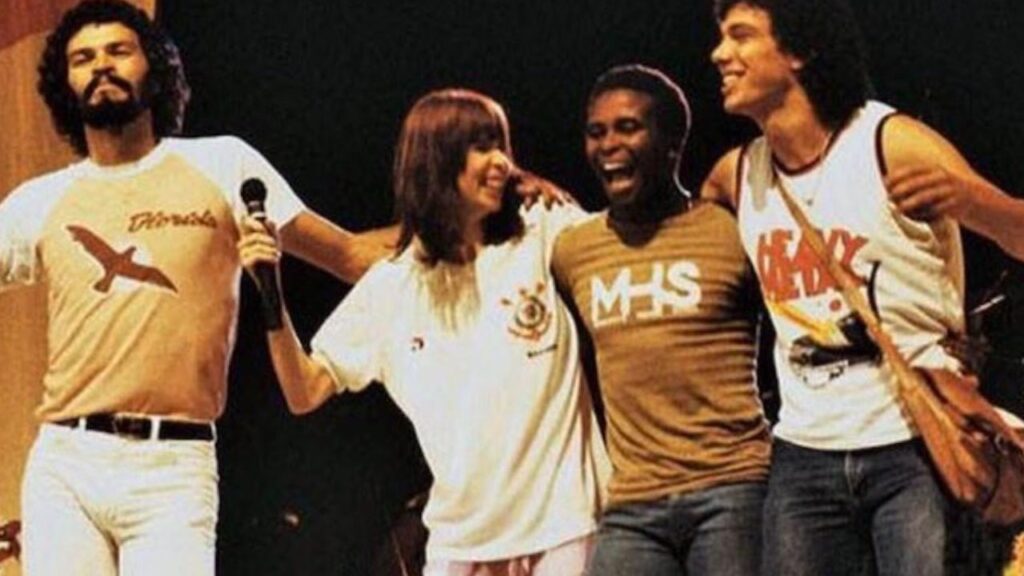 Morre Rita Lee: No palco, Rita Lee segura microfone ao lado de Sócrates, Wladimir e Walter Casagrande