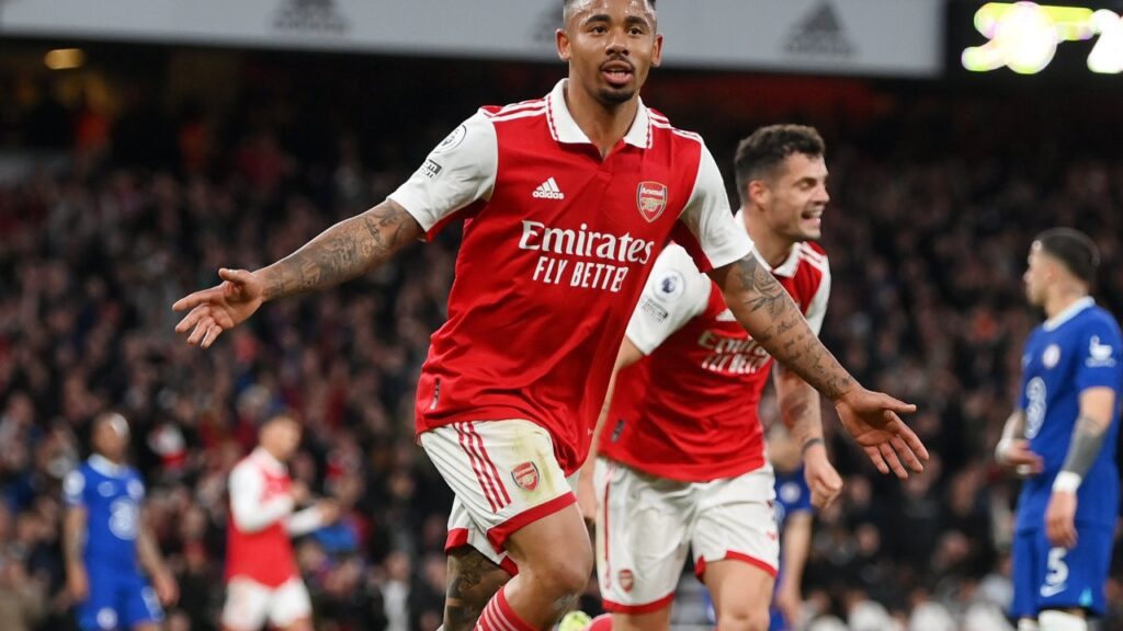 Arsenal e Chelsea duelam e Gunners se mantém na briga pela liderança da Premier League - Gabriel Jesus corre de braços abertos comemorando seu gol pelo Arsenal, na vitória em cima do Chelsea. Ao fundo, um companheiro do brasileiro corre em sua direção, enquanto jogadores do Chelsea lamentam o gol sofrido