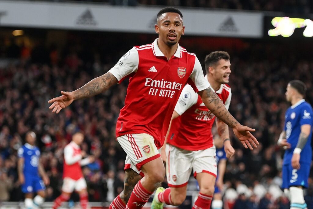 Arsenal e Chelsea duelam e Gunners se mantém na briga pela liderança da Premier League - Gabriel Jesus corre de braços abertos comemorando seu gol pelo Arsenal, na vitória em cima do Chelsea. Ao fundo, um companheiro do brasileiro corre em sua direção, enquanto jogadores do Chelsea lamentam o gol sofrido