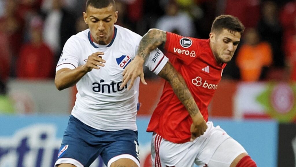 Sofrendo gol nos acréscimos, Internacional empata com o Nacional pela Libertadores - Fabián Bustos, do Internacional, que usa camisa vermelha e calções brancos, está em disputa de bola com jogador do Nacional-URU, que usa camisa branca e calção azul, pela Libertadores.