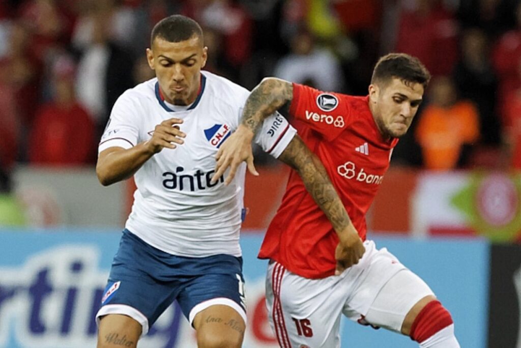 Sofrendo gol nos acréscimos, Internacional empata com o Nacional pela Libertadores - Fabián Bustos, do Internacional, que usa camisa vermelha e calções brancos, está em disputa de bola com jogador do Nacional-URU, que usa camisa branca e calção azul, pela Libertadores.